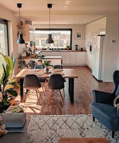 a living room filled with furniture and a dining table next to a kitchen area covered in potted plants