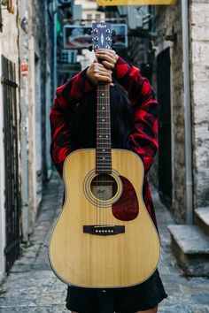 a person with a guitar on their head in an alleyway holding it up to their face