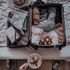 an open suitcase sitting on top of a bed next to a cup of coffee and shoes