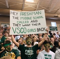 a group of people holding up signs and wearing green face paint at a sporting event