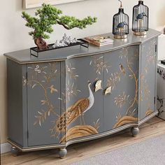 a grey cabinet with birds painted on it and some plants in the top shelf next to it