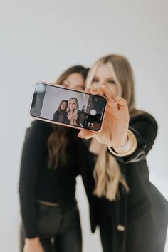 two women are taking a selfie with their cell phone in front of the camera