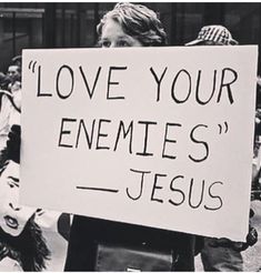 a woman holding a sign that says love your enemies jesus