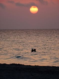 the sun is setting over the ocean with two people swimming in the water at sunset