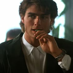 a young man is eating something with his hand and looking at the camera while wearing a black blazer