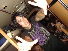 a man with long black hair and tattoos on his arm holding up two fingers in the air