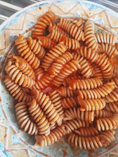 a bowl filled with pasta and sauce on top of a tiled table next to a window