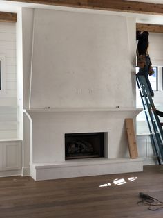 a man on a ladder working on a fireplace in a room with white walls and wood floors