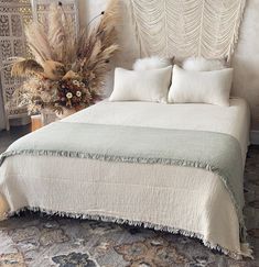 a bed with white linens and pillows on top of it next to a plant