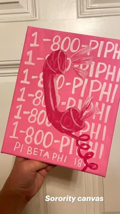 a hand holding up a pink canvas with numbers and letters painted on it, in front of a door