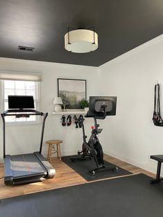 a home gym with treadmills and exercise bikes in the corner, along with a flat screen tv mounted on the wall