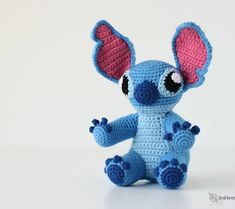 a small crocheted blue and pink stuffed animal with big ears sitting on a white surface