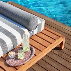 an outdoor table with two drinks on it next to a swimming pool and wooden decking