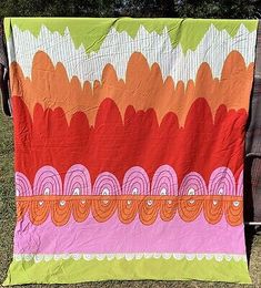 a person holding up a colorful quilt on the grass with trees in the back ground