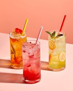 three different types of drinks sitting next to each other on a white table with pink background