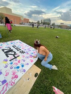 a woman sitting on top of a lush green field next to a large sign covered in handprints