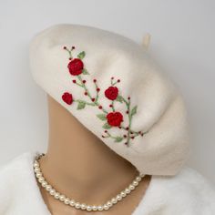 a white hat with red flowers and pearls on the front is adorned with a pearl necklace