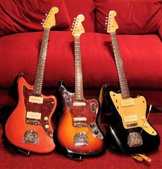 three electric guitars are lined up on a red carpeted floor next to a couch