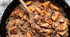 a skillet filled with chicken and mushrooms covered in gravy next to a wooden spoon