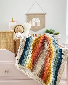 a crocheted blanket sitting on top of a dresser next to a stuffed animal