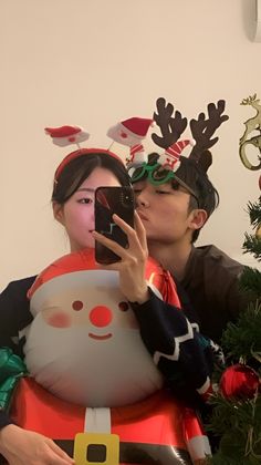 a man and woman taking a selfie in front of a christmas tree with an inflatable santa clause