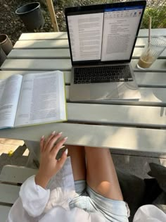 a woman sitting at a table with an open book and laptop computer on her lap