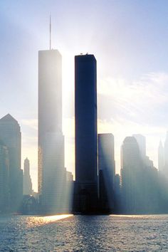 the sun shines brightly in front of two tall buildings on the water's edge