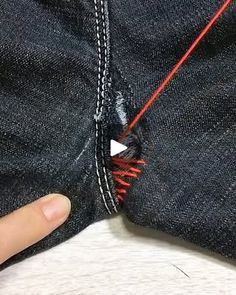 someone is stitching the red thread on their jean pants with one thumb and two fingers