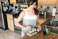 a woman standing in front of a kitchen counter with jars on top of the counter