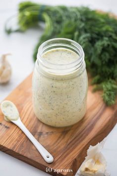 a jar filled with dressing sitting on top of a wooden cutting board next to garlic and parsley