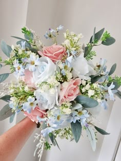 a bridal bouquet with blue and pink flowers on the bride's arm in front of a white wall