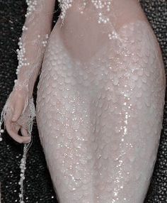 a woman's body is covered in white beads and pearls, as she sits on the floor