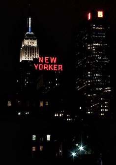 the words new york are lit up at night in front of tall buildings and skyscrapers