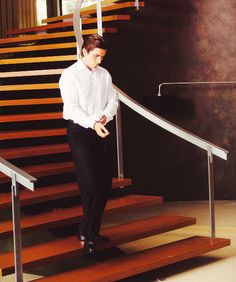 a man in a white shirt and black pants walking up some stairs with his hand on the railing