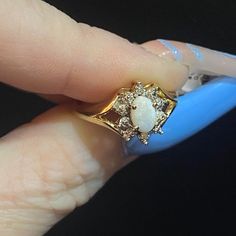 a woman's hand holding a ring with a white stone and diamond accents on it