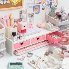 a desk with many items on it and a person pointing at the contents in their drawer