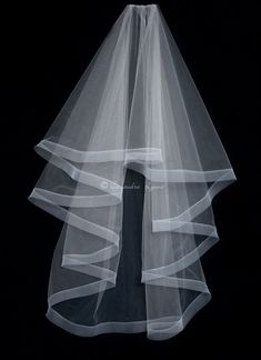 a white veil is hanging on a black wall in front of a dark background with flowers