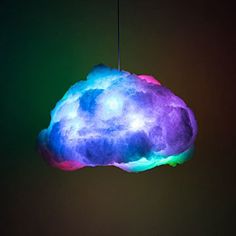 a colorful cloud shaped light hanging from a string in front of a black wall with green and blue lights