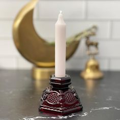 a white candle sitting on top of a black table next to a gold vase and other items