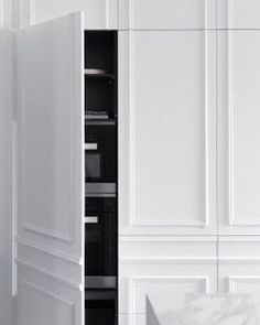 an open cabinet in a white kitchen with marble counter tops and floor to ceiling cabinets