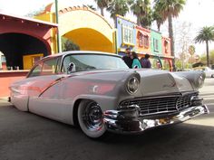 an old car parked in front of a colorful building with palm trees on the side