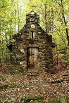 an old stone building in the woods surrounded by leaves and trees with a clock on it's roof