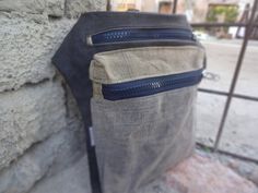 the back pocket of a bag with zippers on it, sitting next to a stone wall