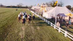 several people are riding horses in an open field with tents on either side of them