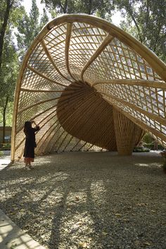 a woman standing in front of a large bamboo structure on top of a dirt field