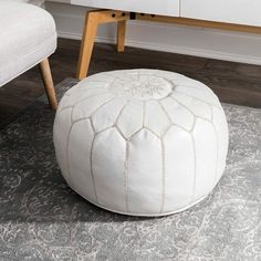 a white ottoman sitting on top of a rug next to a wooden table and chair