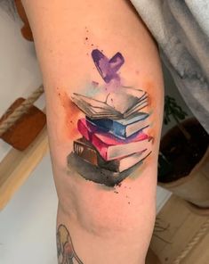 a watercolor painting style tattoo on the leg of a woman's arm with books