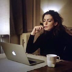 a woman sitting at a table with a laptop and coffee cup in front of her