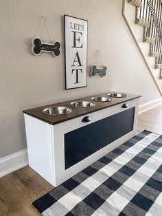 a dog's kennel with two bowls on the floor and a sign above it that says let's eat