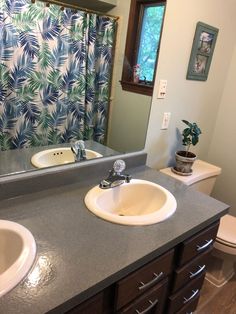 a bathroom with two sinks and a shower curtain in the window above it is a blue palm leaf print shower curtain